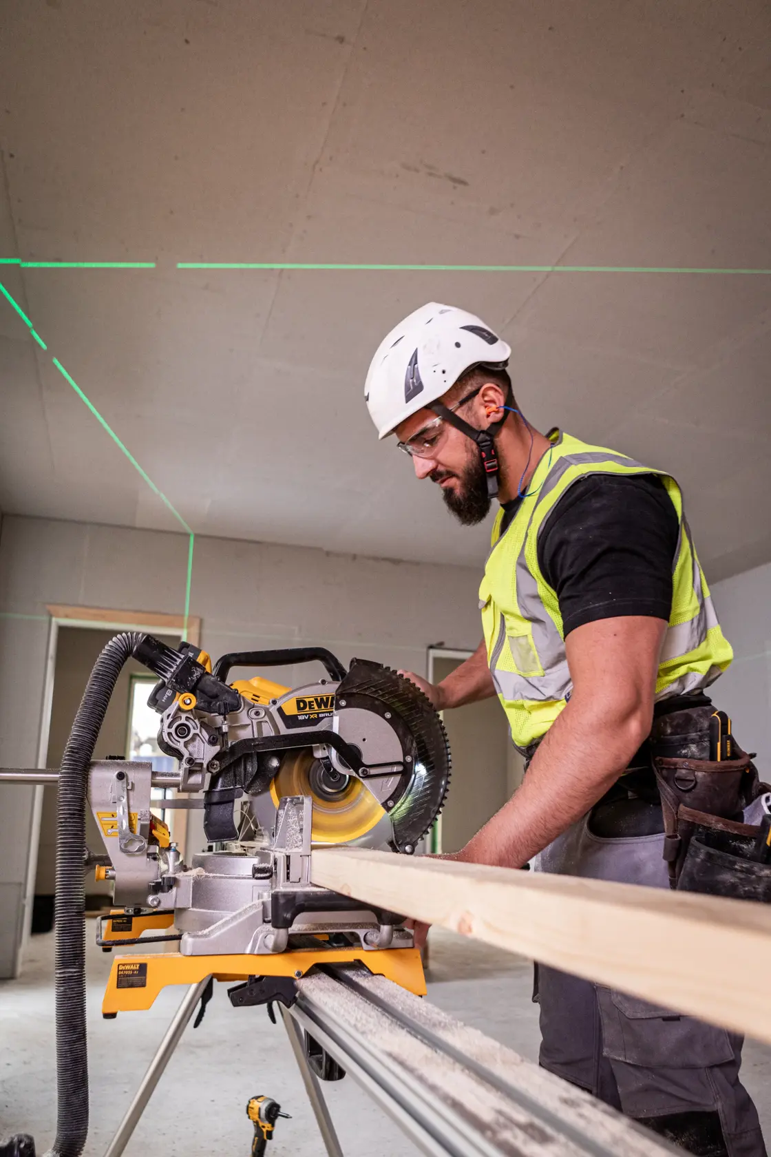 Trabajador corta madera con DEWALT DCS782N; lleva protección y se ven guías láser.