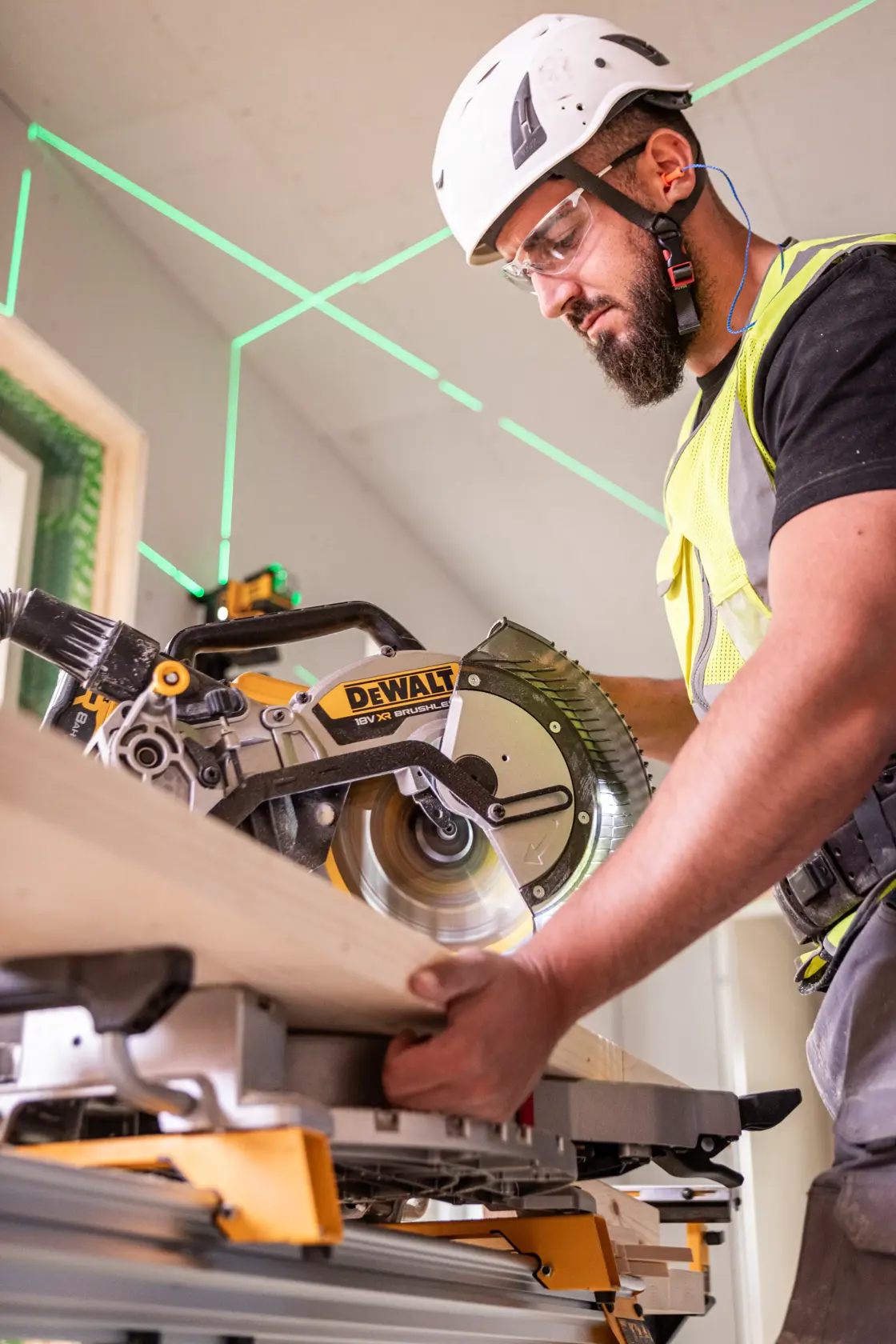 Trabajador corta madera con una DEWALT DCS782N, usando casco y chaleco de seguridad en interior.