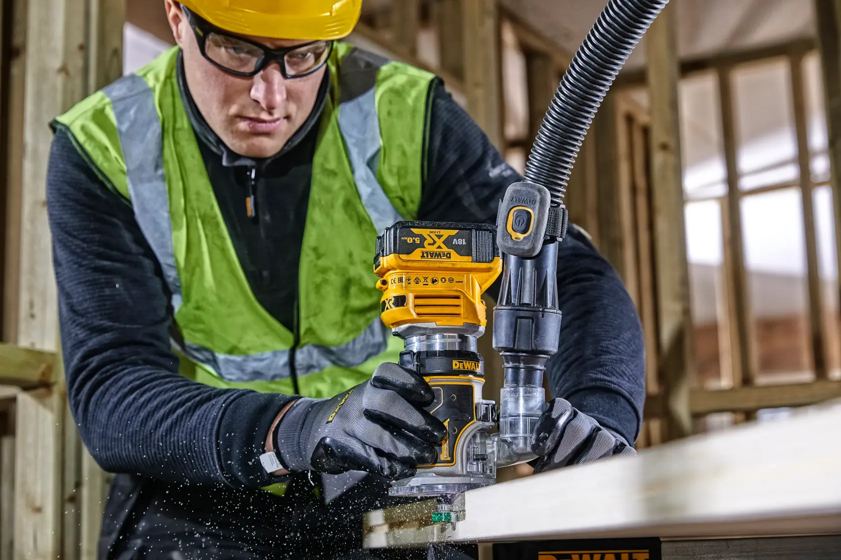 Une personne façonne du bois avec une défonceuse DEWALT DCW604, portant des équipements de sécurité sur un chantier.