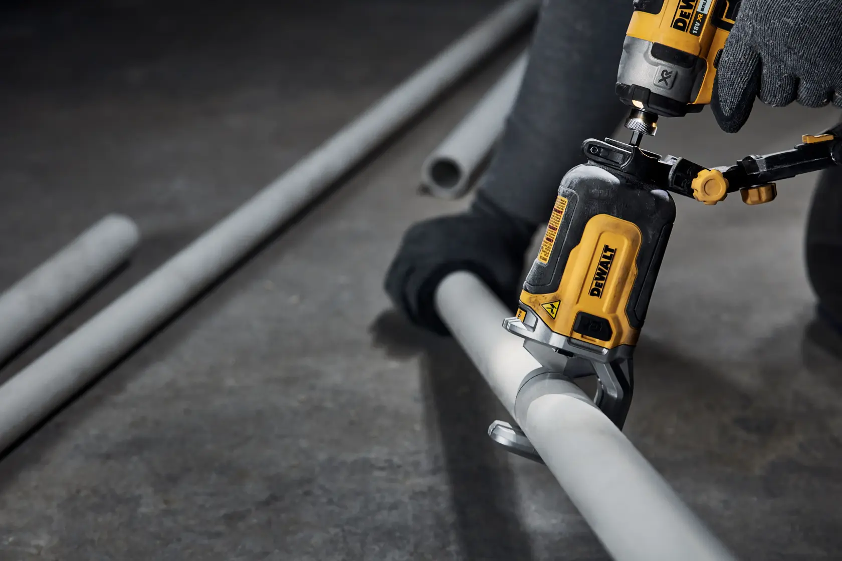 Primer plano de una herramienta eléctrica DEWALT utilizada por una persona con guantes para cortar un tubo de metal gris en el suelo de un taller.