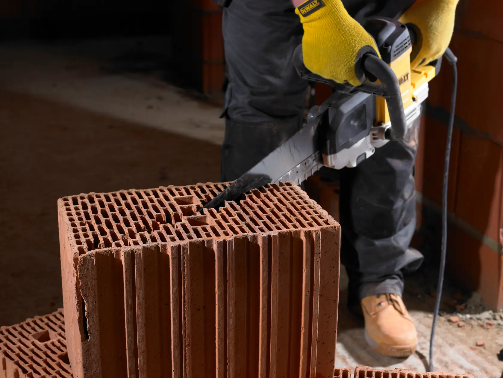 Person schneidet hohlen Ziegel mit DEWALT Säge auf Baustelle.