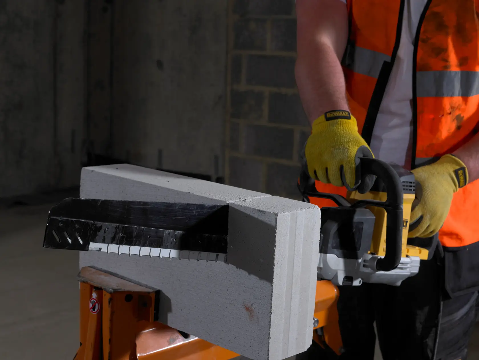 Person schneidet drinnen einen Betonblock mit einer DEWALT Säge und Handschuhen.
