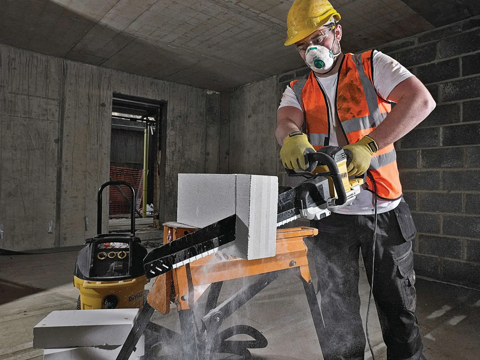 Arbeiter schneidet Betonblock mit DEWALT Werkzeug drinnen, trägt Weste, Handschuhe und Helm.