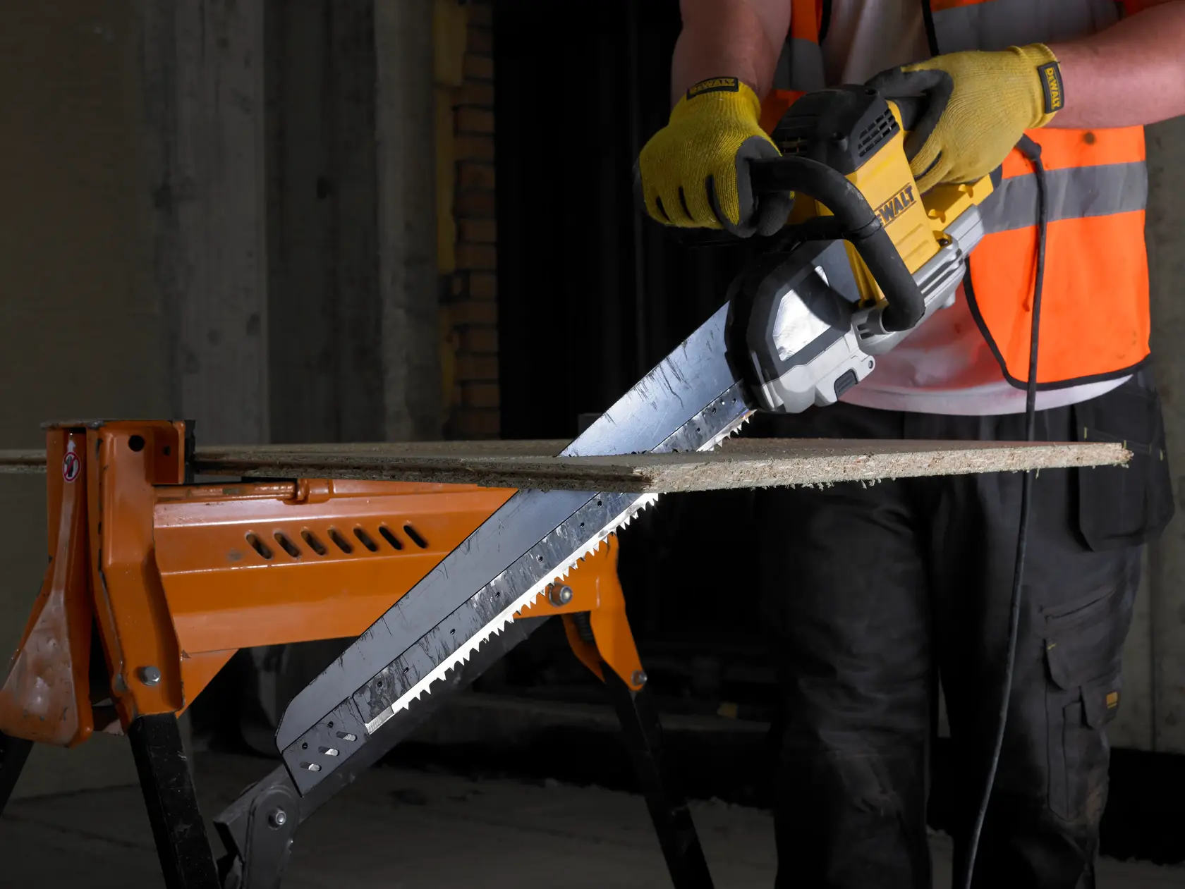 Person sägt Holz mit einer DEWALT Elektro-Säge, trägt Handschuhe und Weste, Holz auf orangener Werkbank.