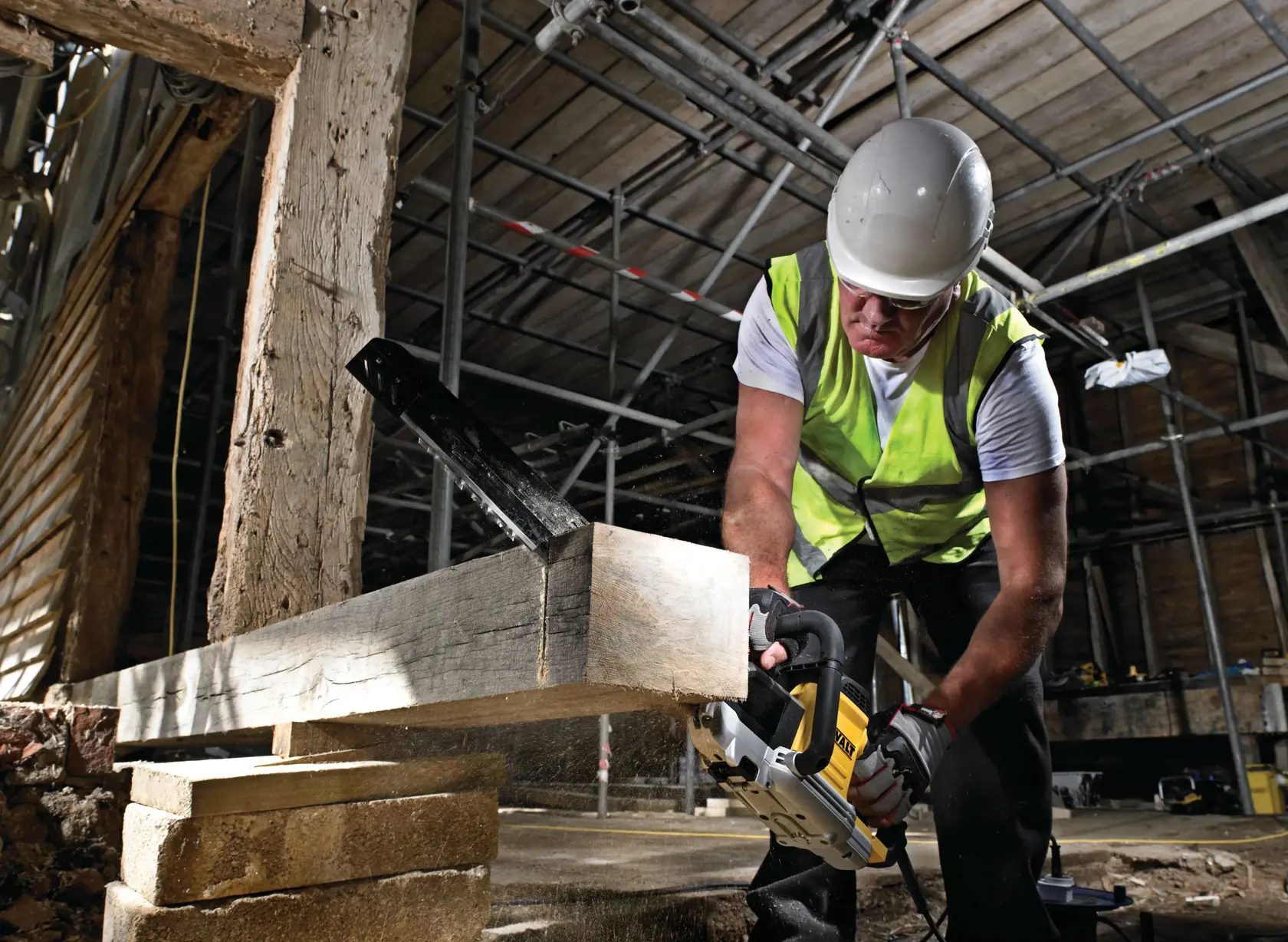 Arbeiter mit Schutzkleidung schneidet mit einer DEWALT Säge einen Holzbalken auf der Baustelle.