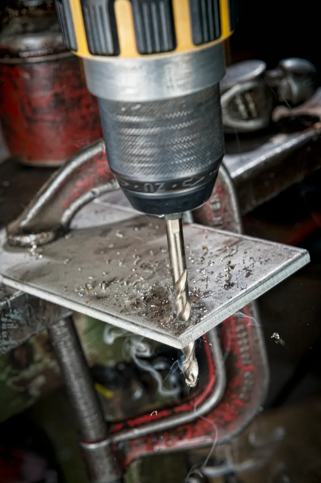 Un taladro con broca DEWALT perfora una placa metálica sujeta a un banco de trabajo.