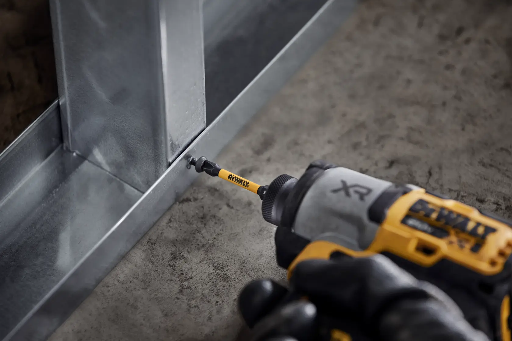 DEWALT power tool with screwdriver bit attaching metal frame on concrete floor.