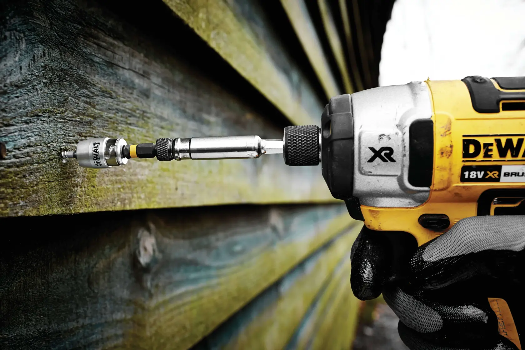 DEWALT drill driving a screw into wooden siding, close-up view of tool in action.