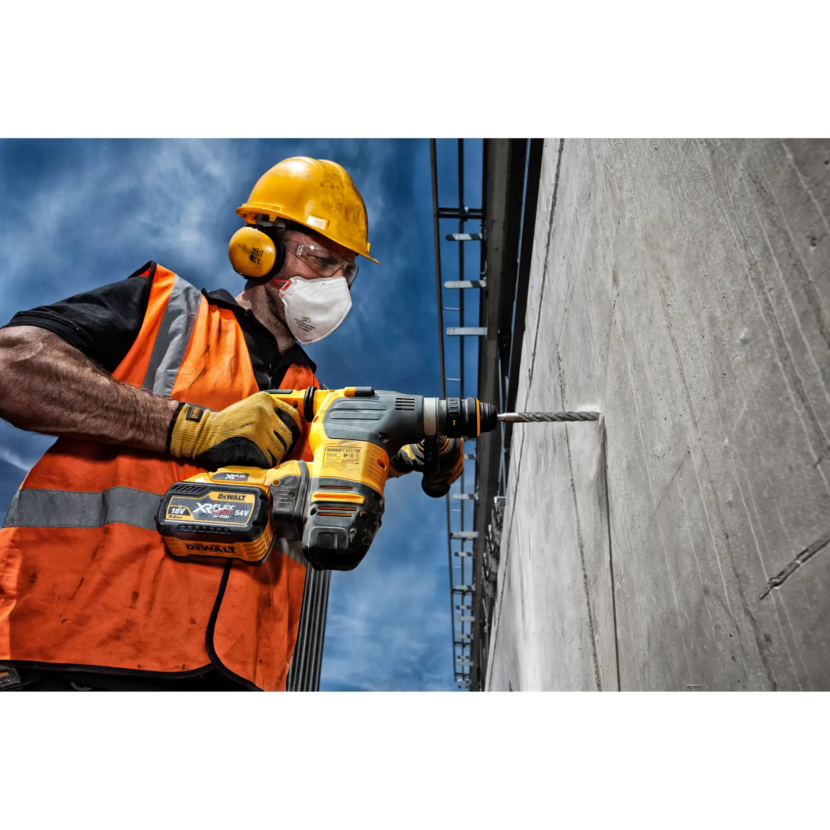 Trabajador perfora pared de concreto con DEWALT DT9515, usa equipo de seguridad y chaleco naranja.