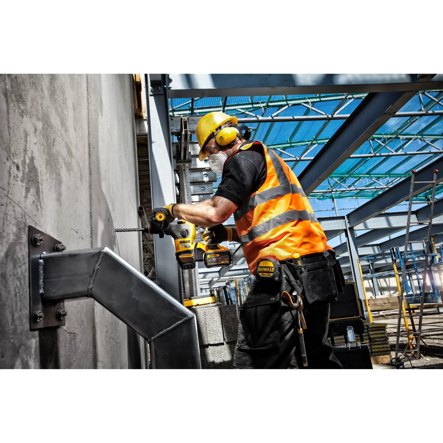 Trabajador usa un taladro DEWALT en muro de cemento, lleva chaleco naranja y equipo de seguridad.