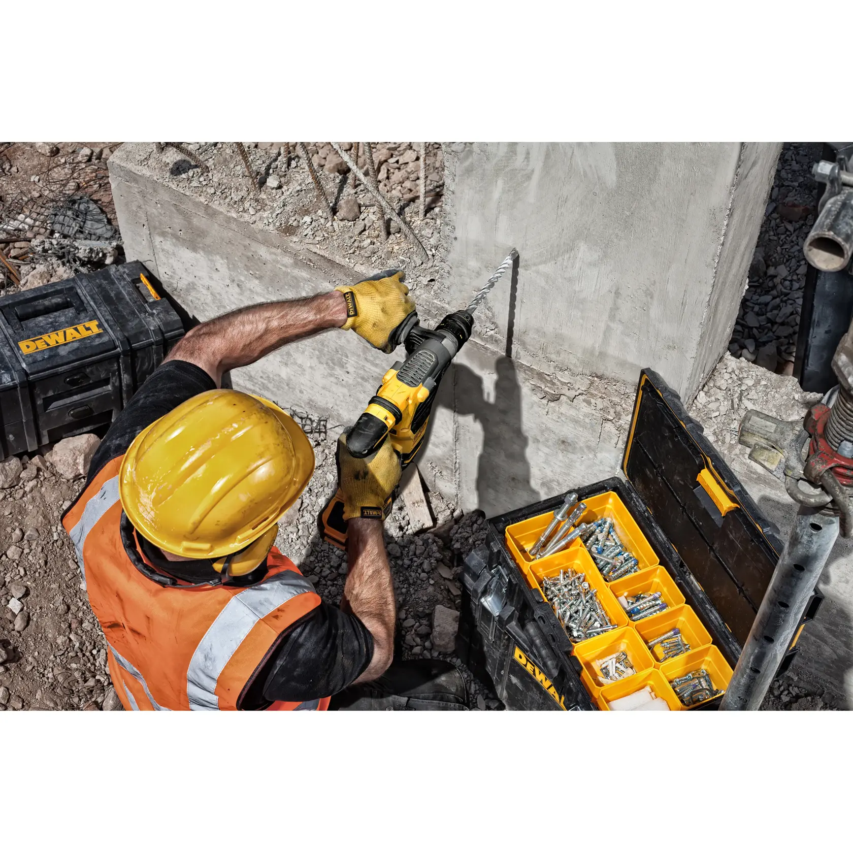 Trabajador perfora concreto con herramienta DEWALT, usando tornillos de caja amarilla y negra en obra.