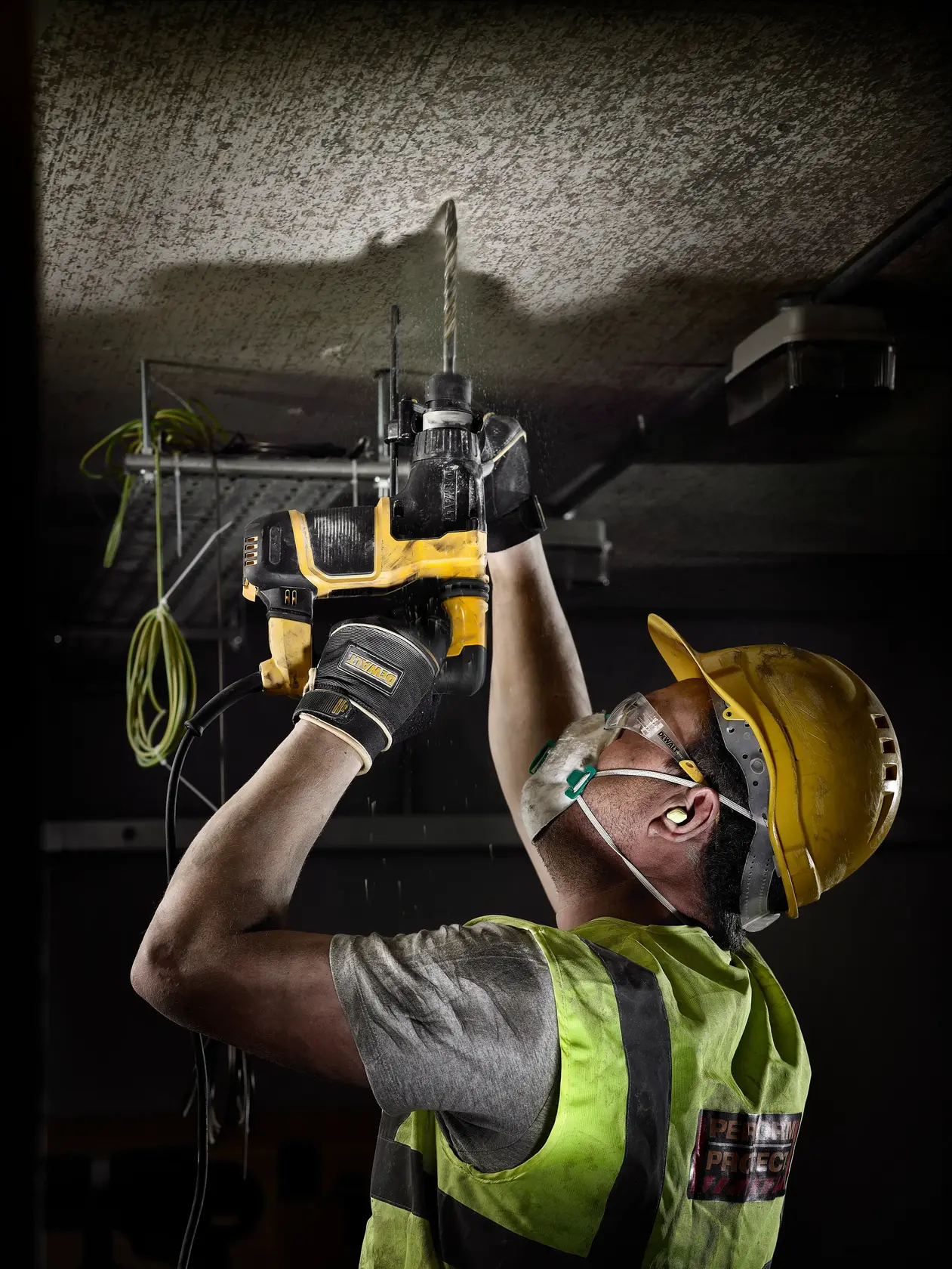 Photo of DEWALT DT9574 worker drilling ceiling, wearing safety gear. Yellow drill visible. Construction environment.