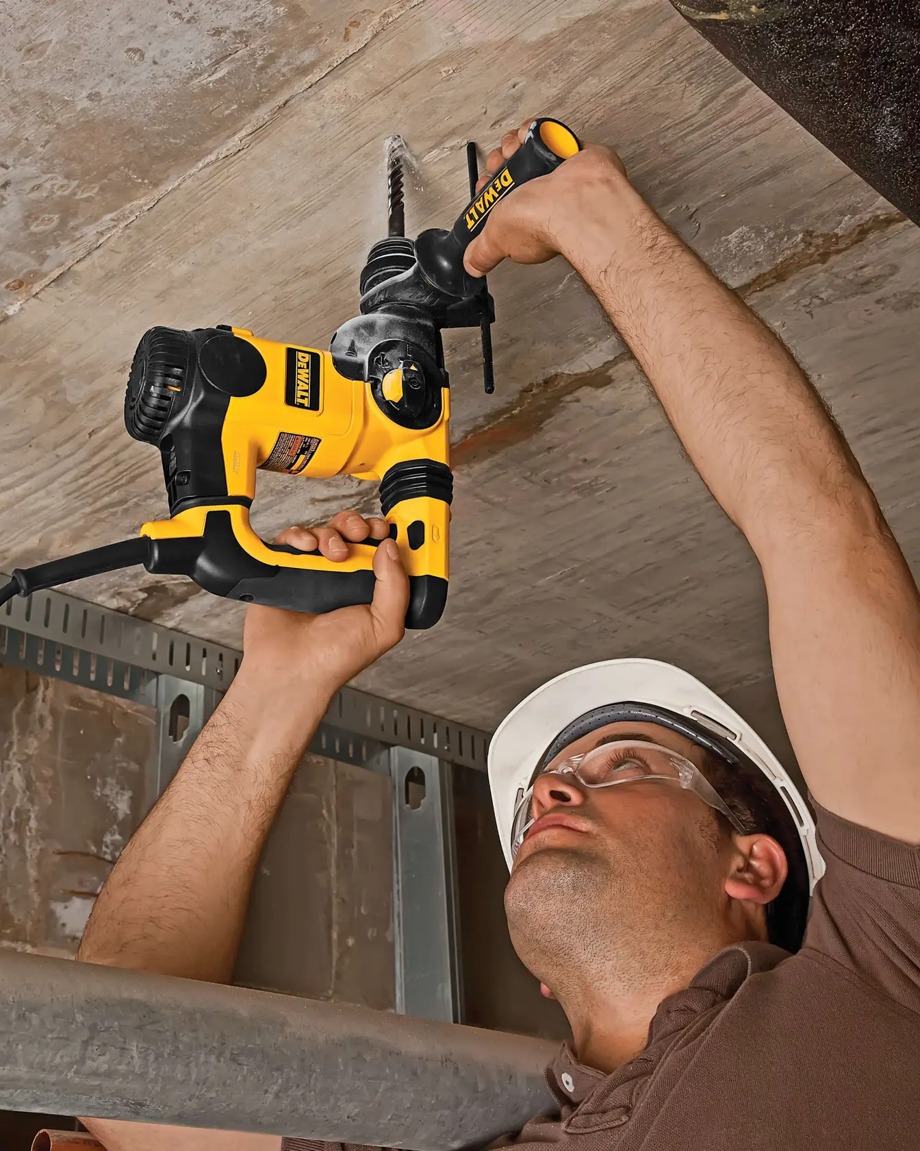 Person using a DEWALT power drill to drill into a concrete ceiling while wearing safety gear.